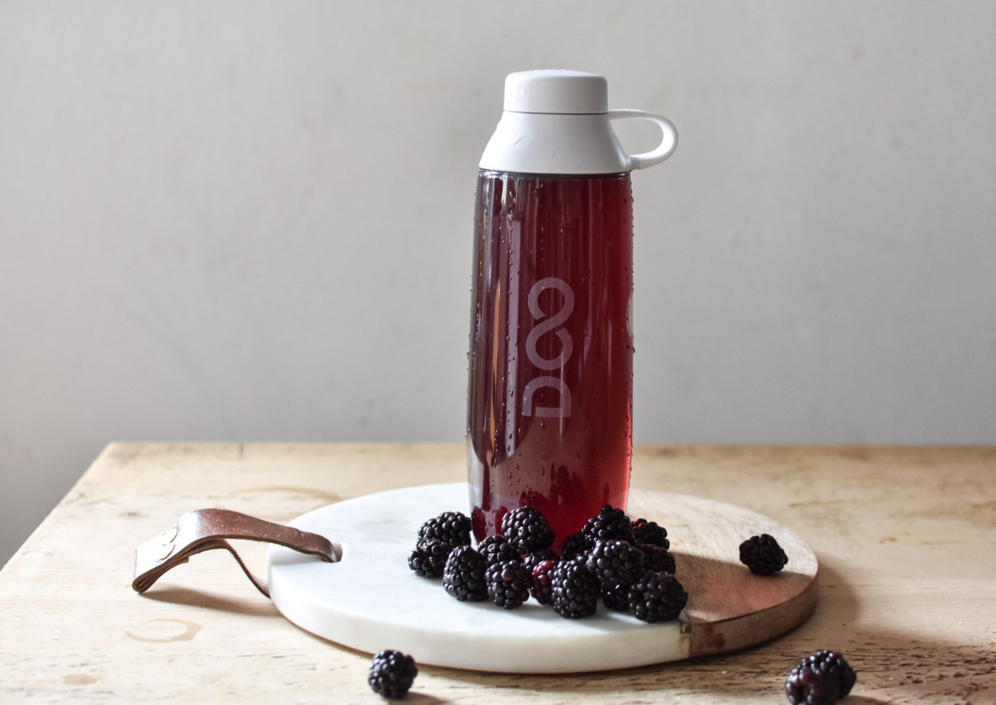 Drinkfinity reusable bottle filled with Charge Pod surrounded by blackberries
