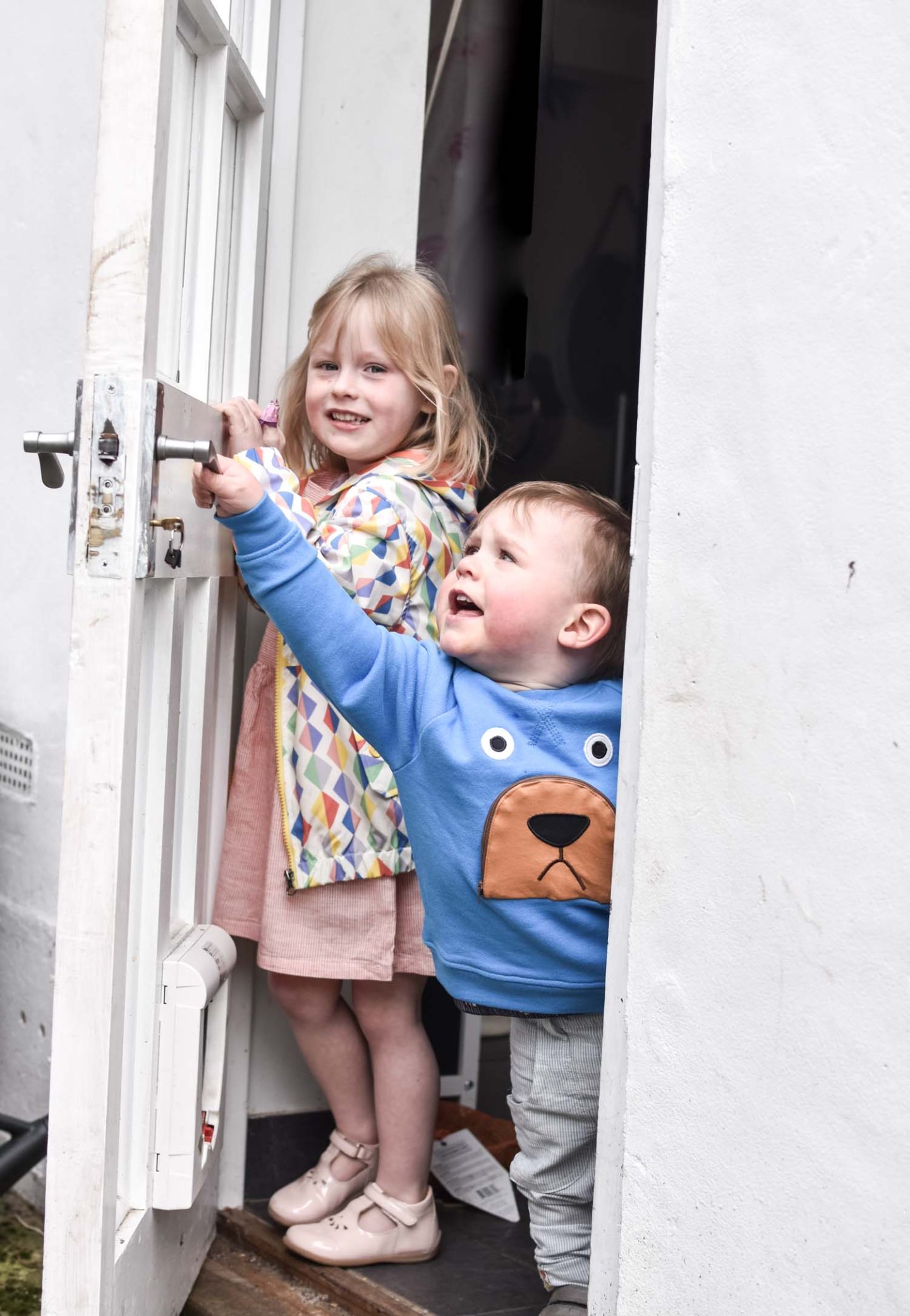 Daisy wears a smock dress and diamond print rain coat, Laurie wears a bear jumper and linen trousers from Tootsa MacGinty