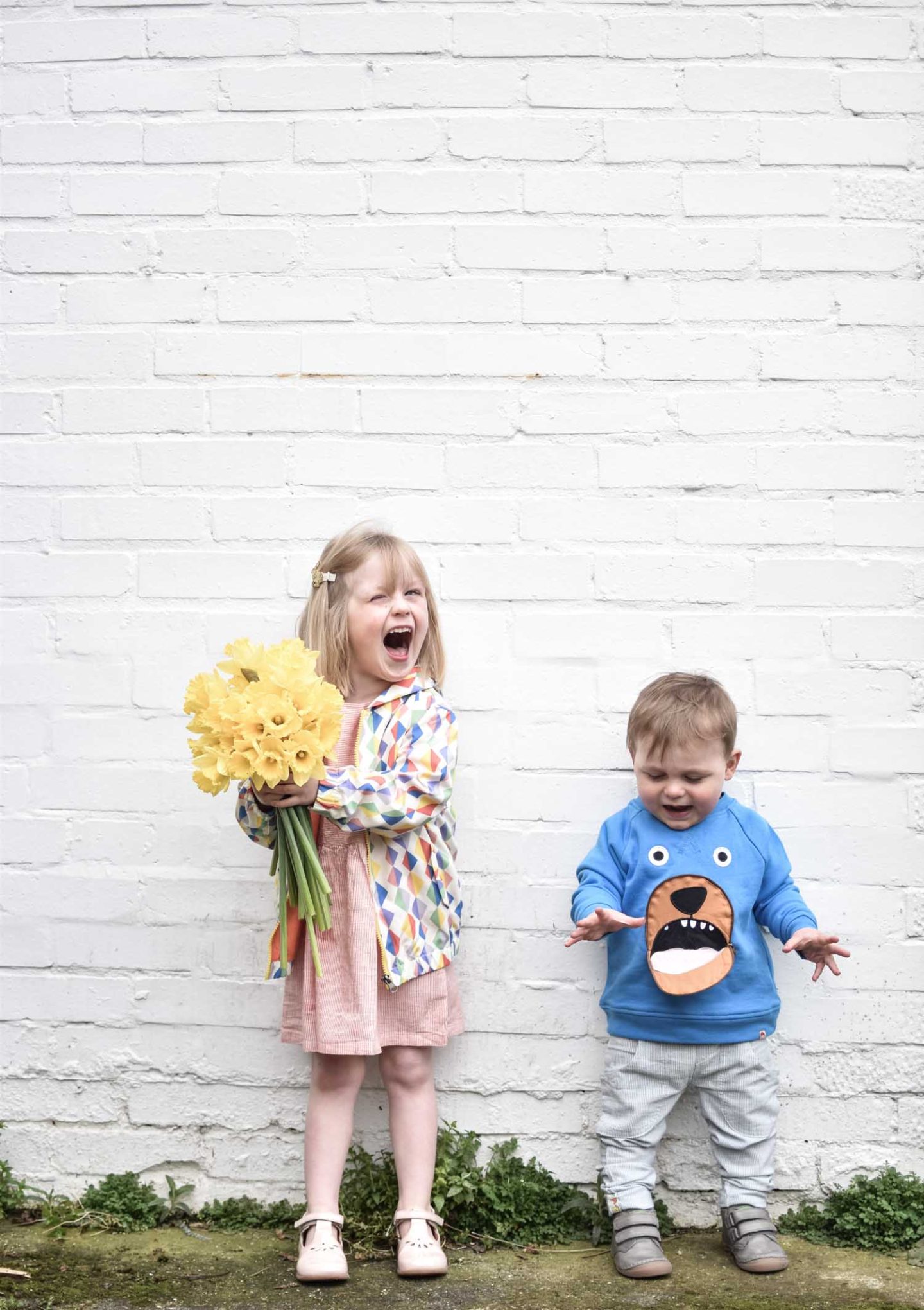 Daisy wears a smock dress and diamond print rain coat, Laurie wears a bear jumper and linen trousers from Tootsa MacGinty