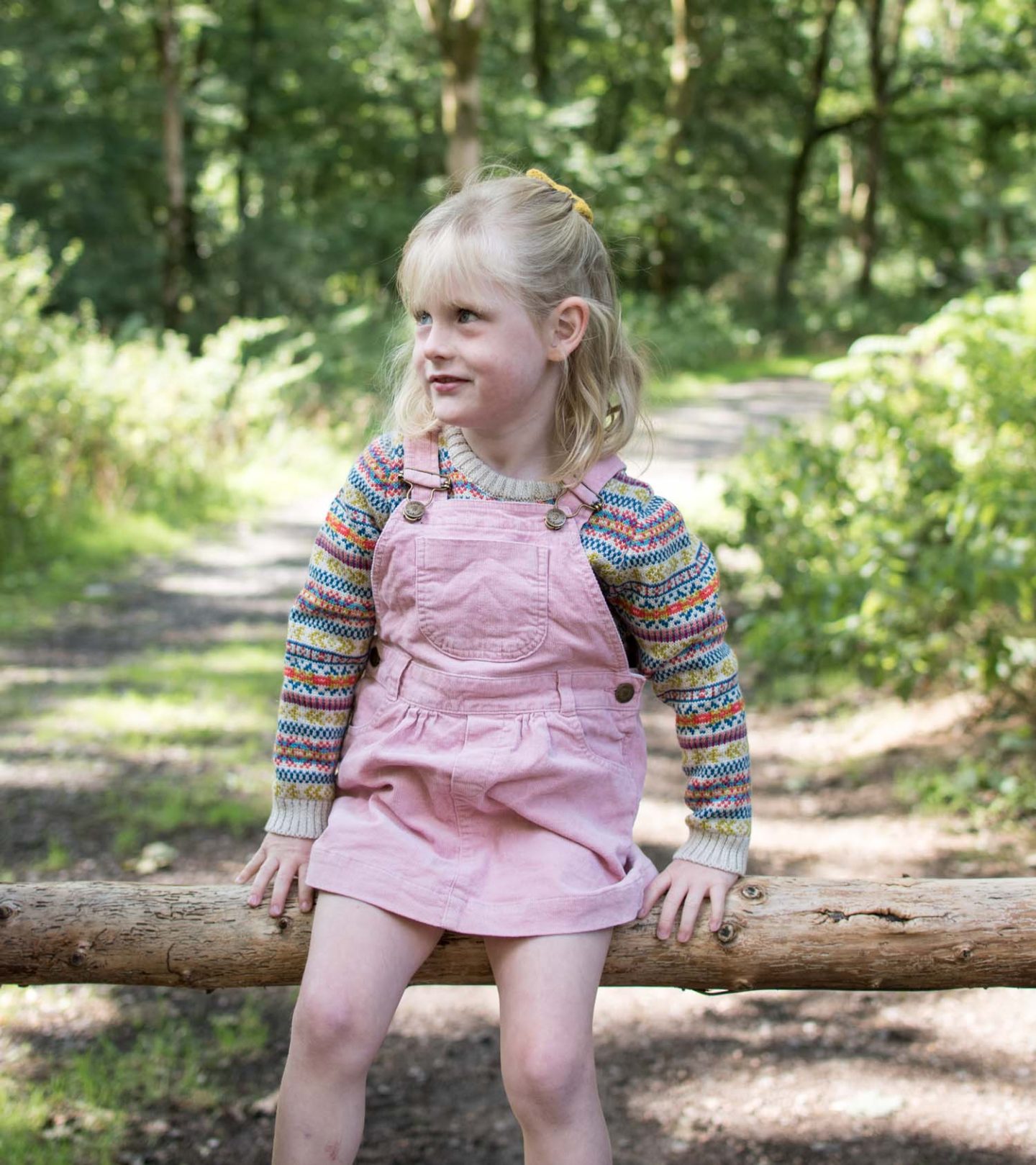 Daisy in the forest wearing The Faraway Gang explorer jumper with a Dotty Dungaree pink cord pinafore dress