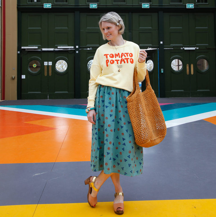 Karen Maurice of n4mummy wearing a yellow sweatshirt and green patterned skirt from ethical fashion brand Bobo Choses with clogs from Kitty Clogs Sweden