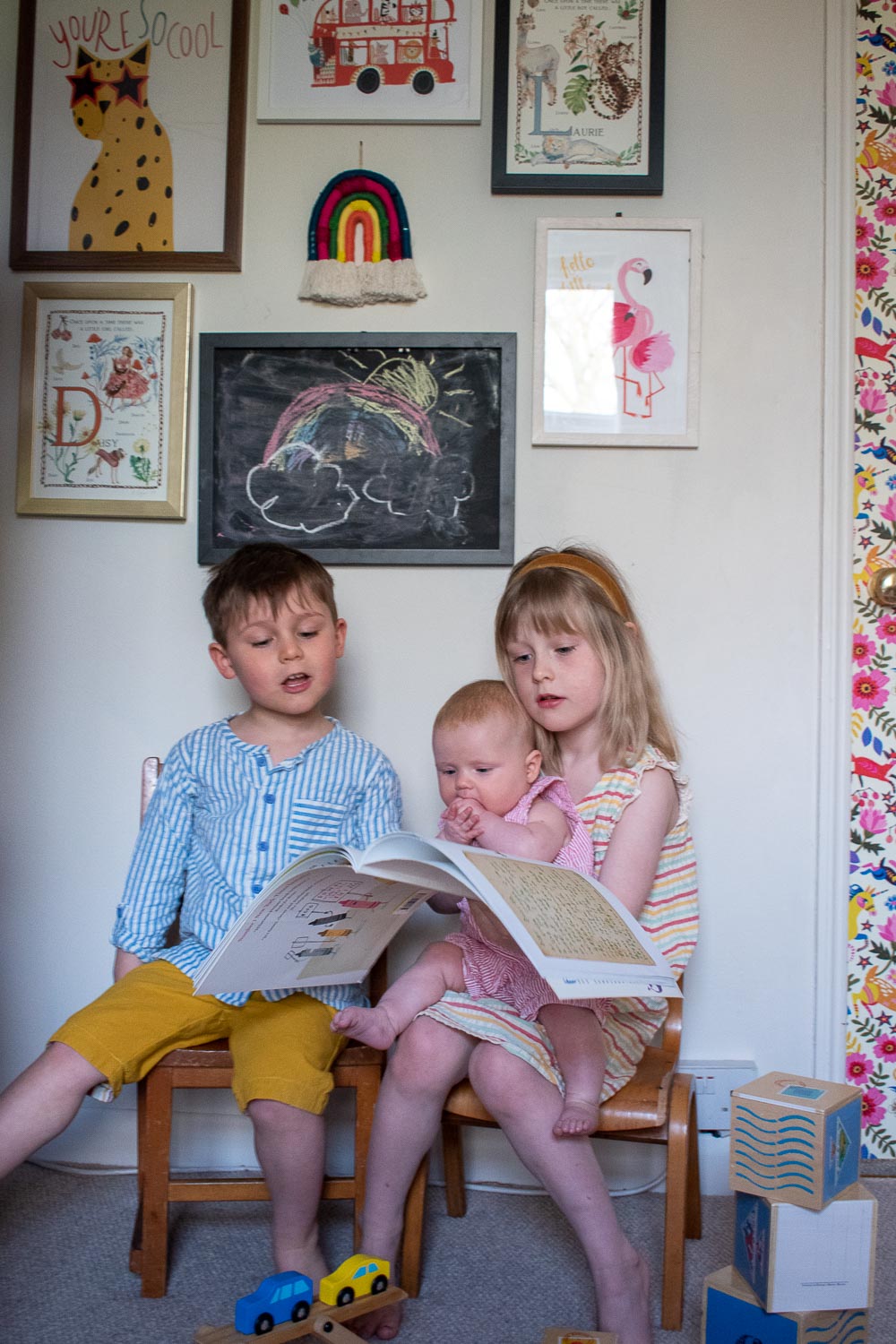 Daisy reading a book to Clara and Laurie, their photo gallery wall behind them with their personalised name pictures from Traces of Magic