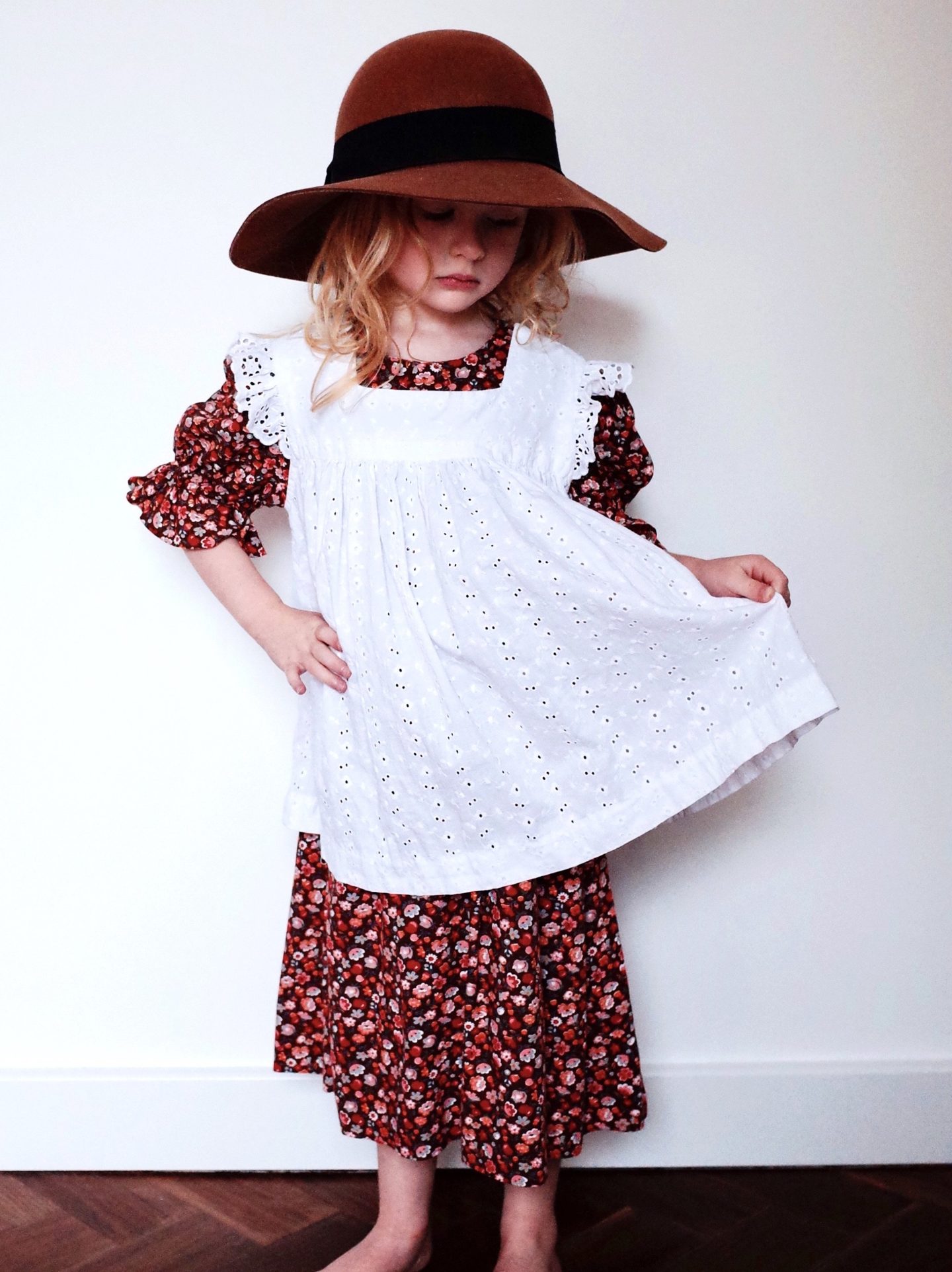 Girl in a floral dress and white pinafore, from second hand childrens clothing brand Wolf & Mabel