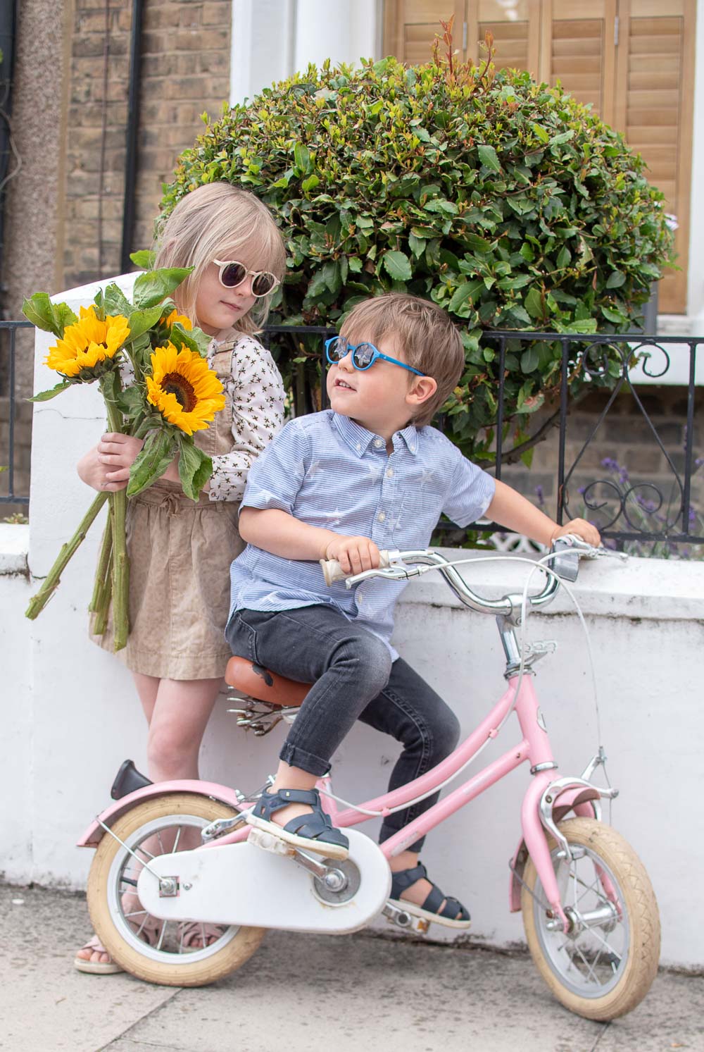 Girl carrying sunflowers and boy on a bike wearing second hand children's clothes from Tot Swap