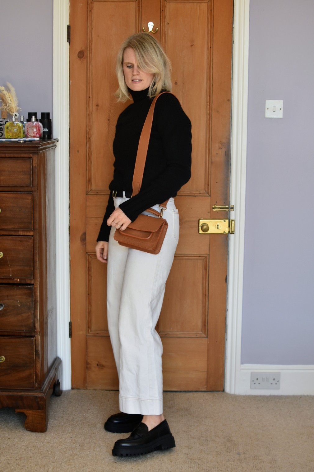 Karen Maurice sustainable influencer wearing a black cashmere jumper from Nearly New Cashmere, white jeans and a tan bag.